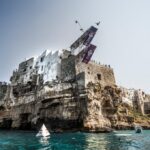 A diver in mid-air from the Red Bull Cliff Diving platform set on the houses above the cliff at Polignano a Mare