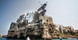 A diver in mid-air from the Red Bull Cliff Diving platform set on the houses above the cliff at Polignano a Mare