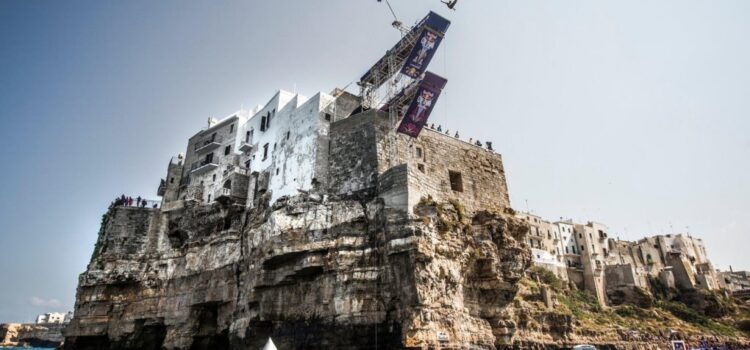 A diver in mid-air from the Red Bull Cliff Diving platform set on the houses above the cliff at Polignano a Mare