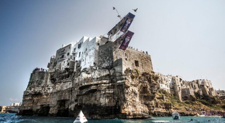 A diver in mid-air from the Red Bull Cliff Diving platform set on the houses above the cliff at Polignano a Mare