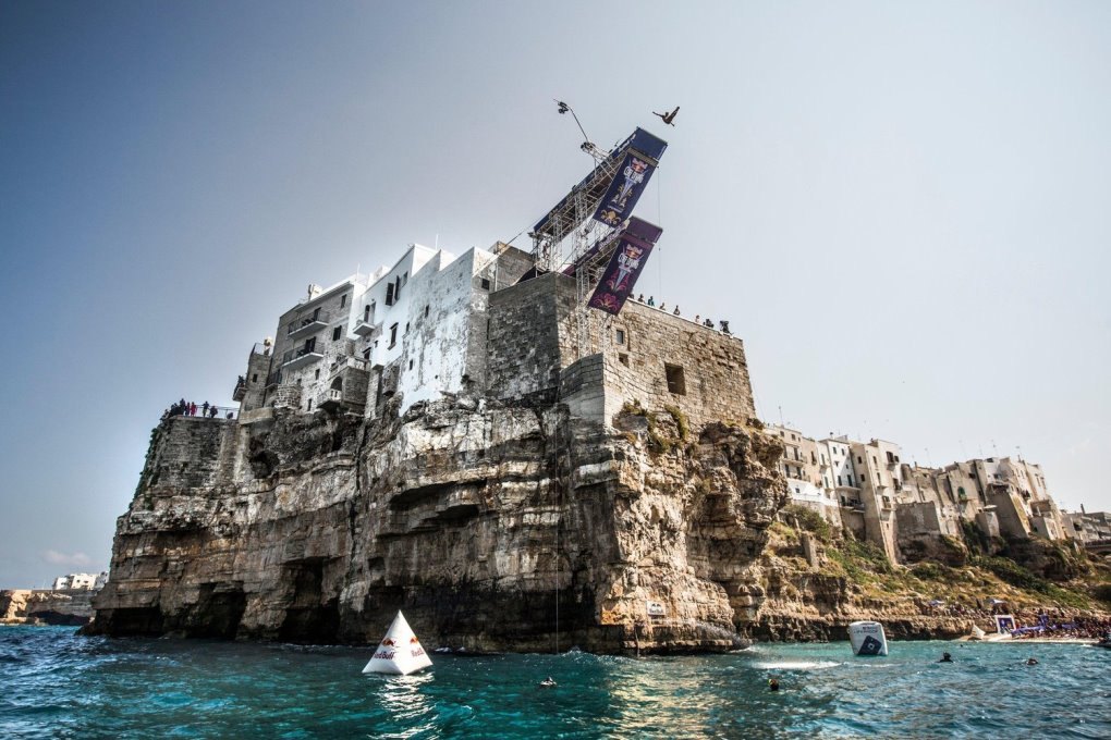 A diver in mid-air from the Red Bull Cliff Diving platform set on the houses above the cliff at Polignano a Mare