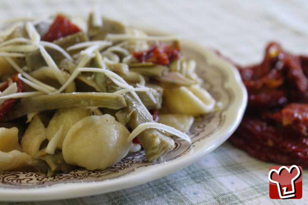 A plate of orecchiette with artichokes, grated cheese and pieces of sun-dried tomato, with more dried tomatoes on the side