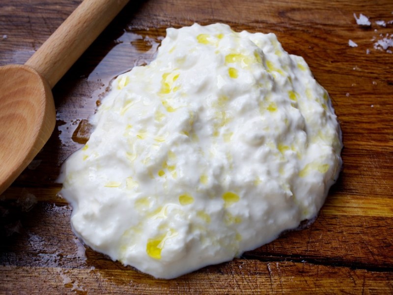 A mound of fresh stracciatella with a drizzle of olive oil on a wooden board, next to a wooden spoon
