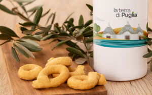 Apulian taralli on a wooden board beside an olive branch and a bottle of La Terra di Puglia olive oil